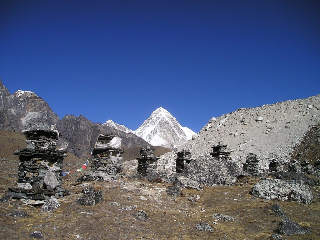 Buddhist stone sculpture with prayer flags in the foreground, set against the majestic backdrop of Mount Everest and the Himalayan range.