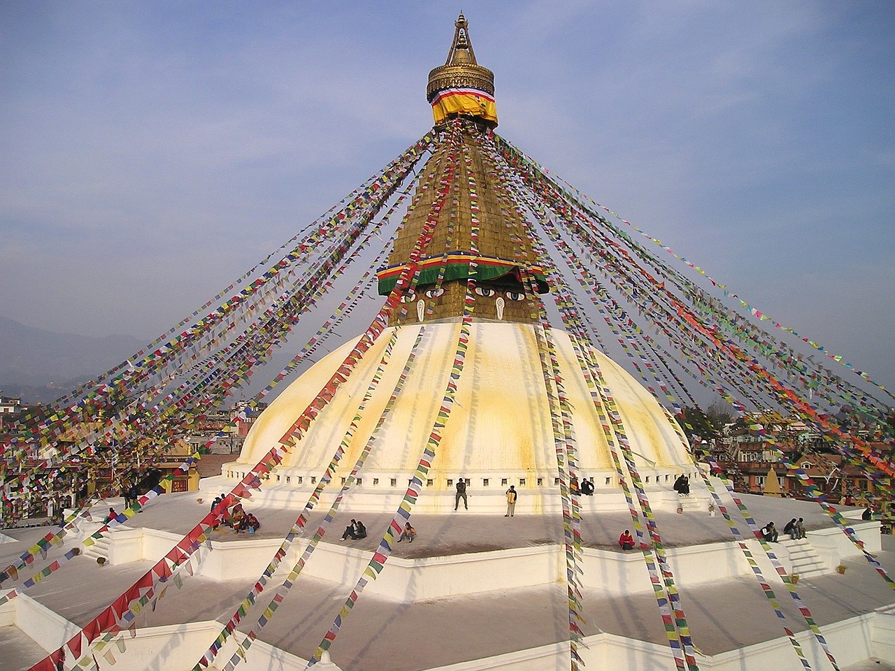 Boudhanath Stupa with white dome, golden spire, and all-seeing eyes of Buddha, surrounded by prayer flags.