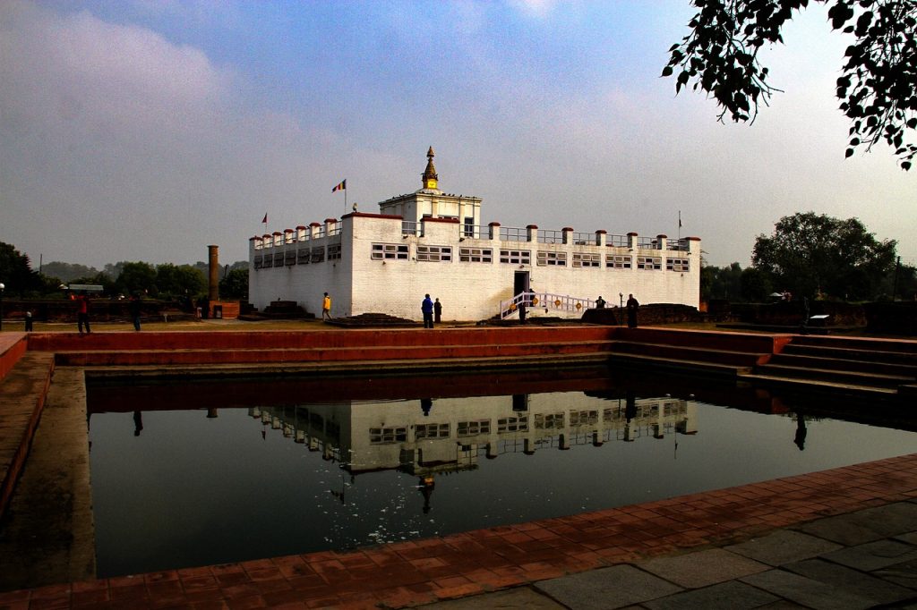 Panoramic view of Lumbini with sacred Bodhi tree, ancient stupas, and prayer flags against a serene sky.