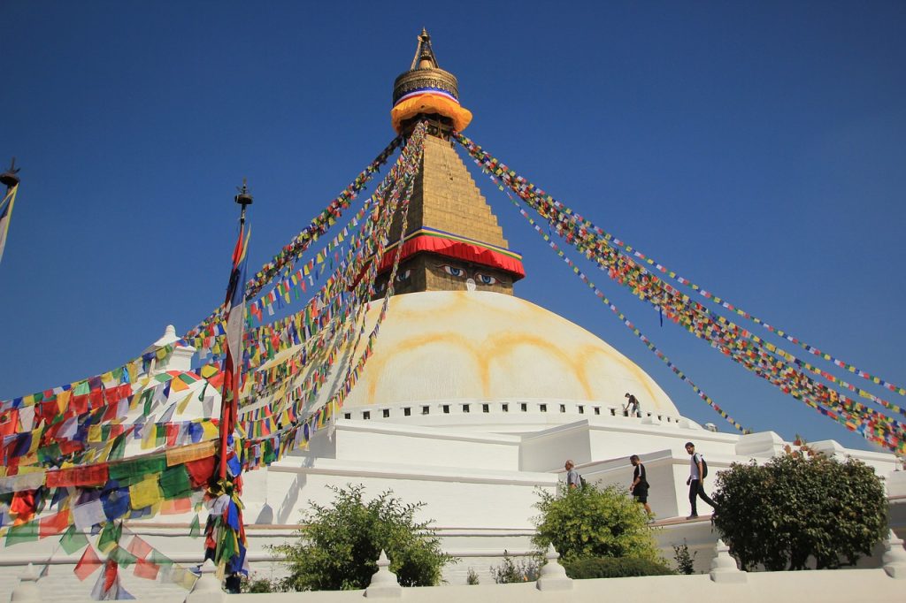 Boudhanath Stupa with colorful prayer flags fluttering in the wind against a clear blue sky.