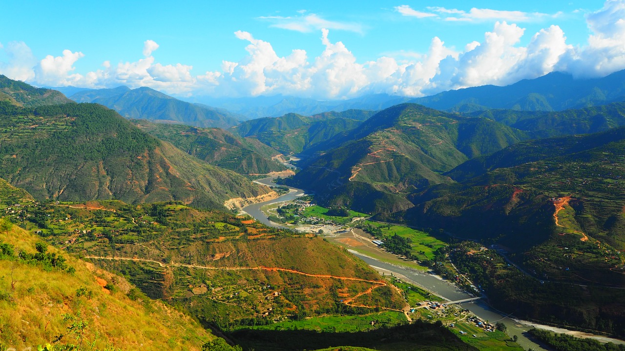 Panoramic view of rolling green hills in the foreground with towering snow-capped mountain peaks in the background.