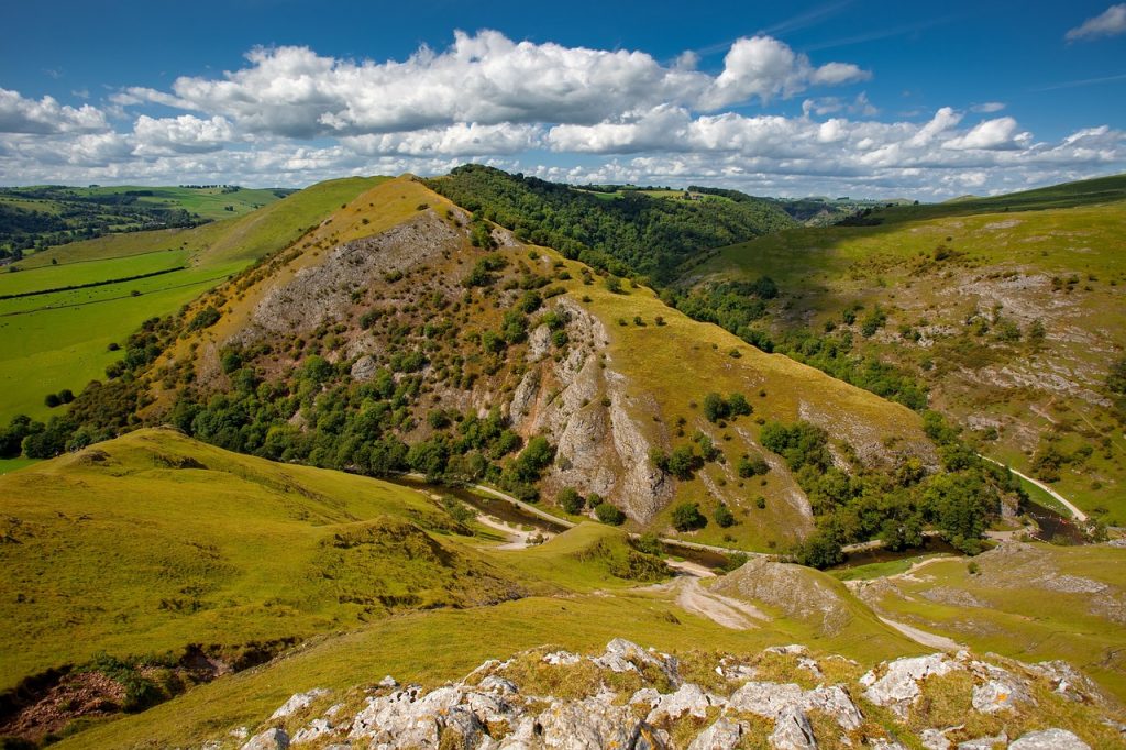 Rolling green hills of Ilam adorned with terraced tea plantations under a soft blue sky with fluffy clouds.
