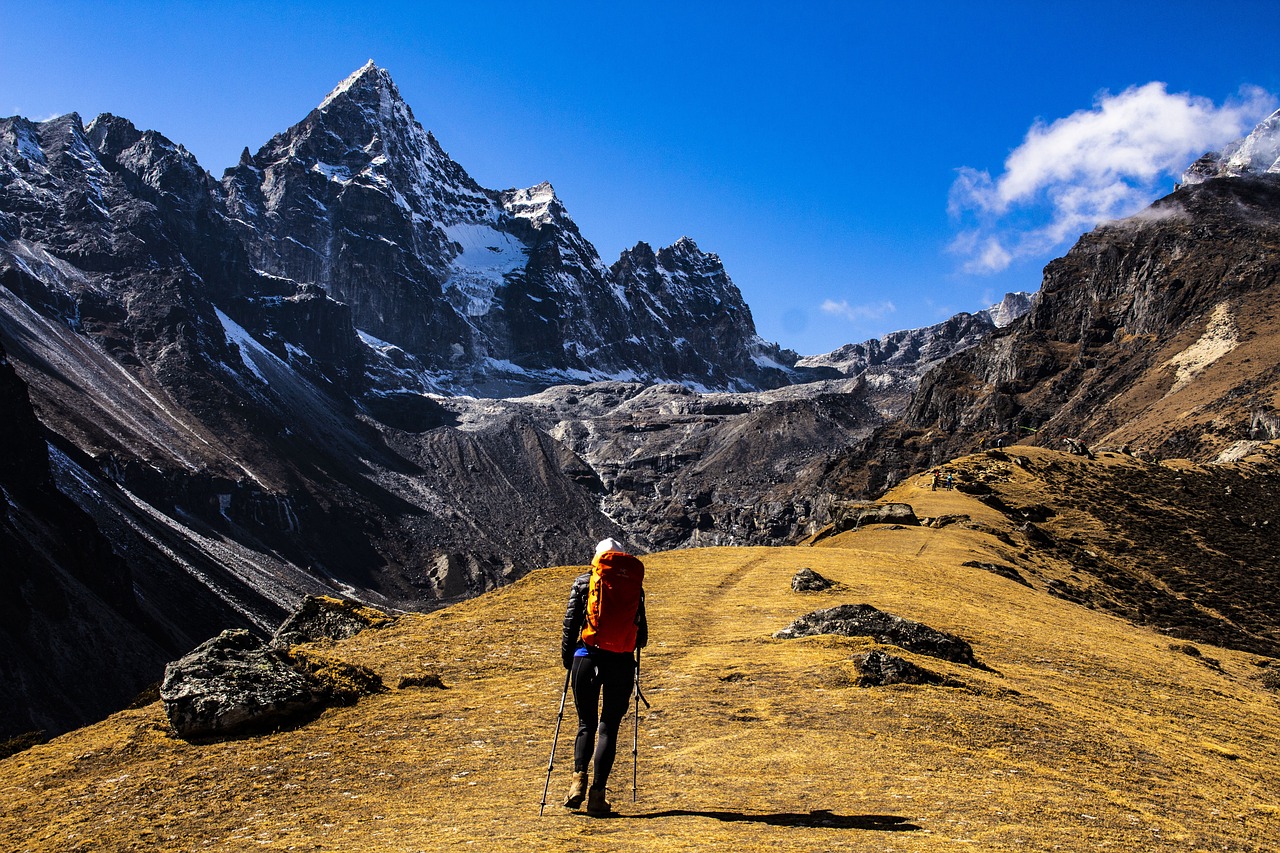 Mount Everest viewed from a winding trail lined with prayer flags, surrounded by rugged Himalayan terrain.