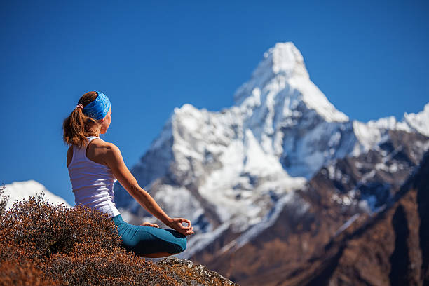 A young woman practicing yoga outdoors in a meditative pose with the Himalaya mountains in the background.