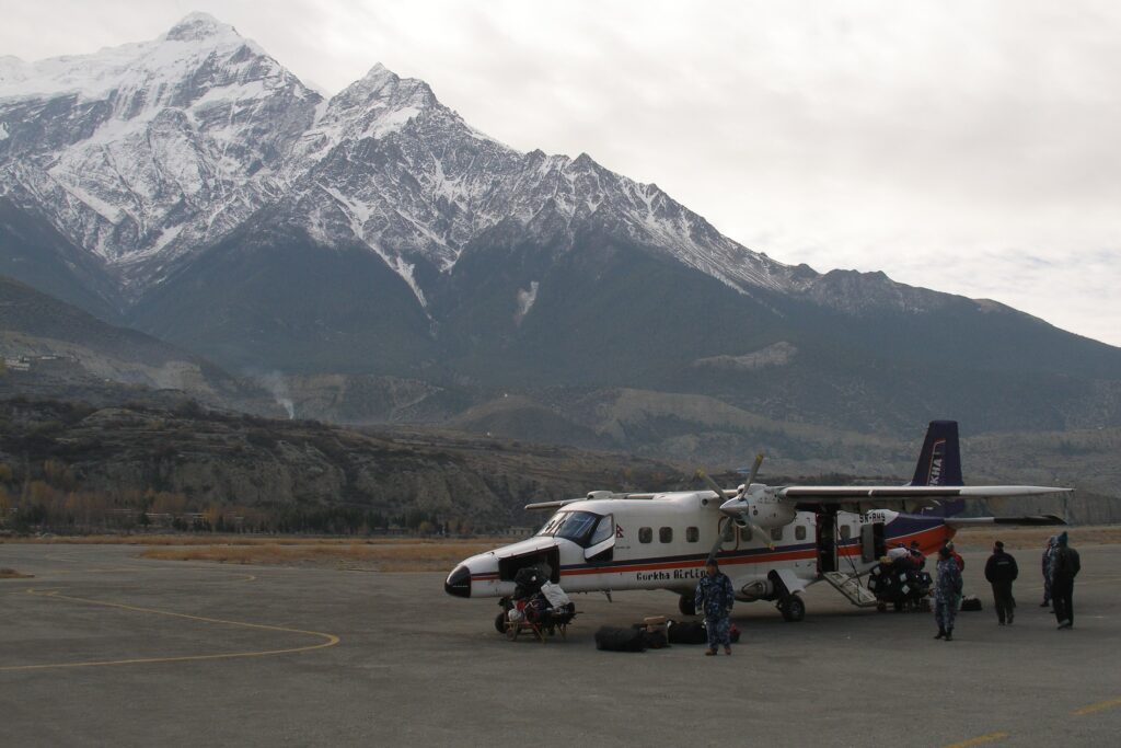 A plane parked at Jomsom Airport with the stunning Annapurna mountain range in the background, as passengers disembark from the aircraft.