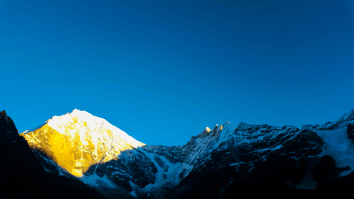 Sunrise over the Langtang Himalayas, with golden light illuminating the snow-covered peaks and a clear sky in the background.