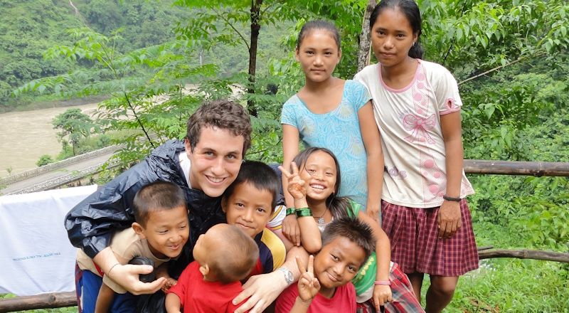 A heartwarming moment captured: a foreign trekker sharing smiles and stories with local students while volunteering in Nepal, bridging cultures through a shared love of learning and adventure.