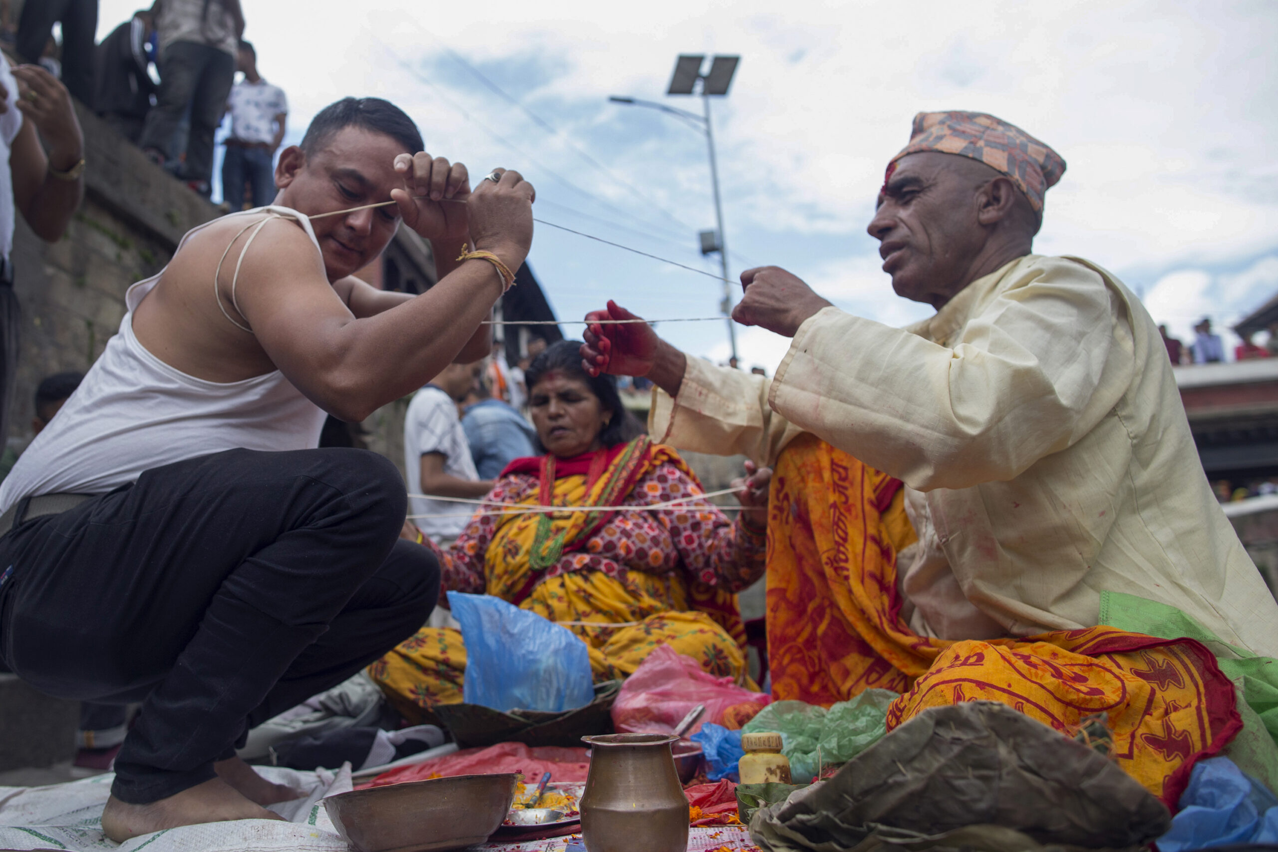 A group of Hindu devotees celebrating Janai Purnima, a sacred festival in Nepal. A priest (Pujari) is seen applying a red tika on a man's forehead while another person removes the old sacred thread (Janai) and wears a new one. The scene is filled with devotion and spiritual significance.