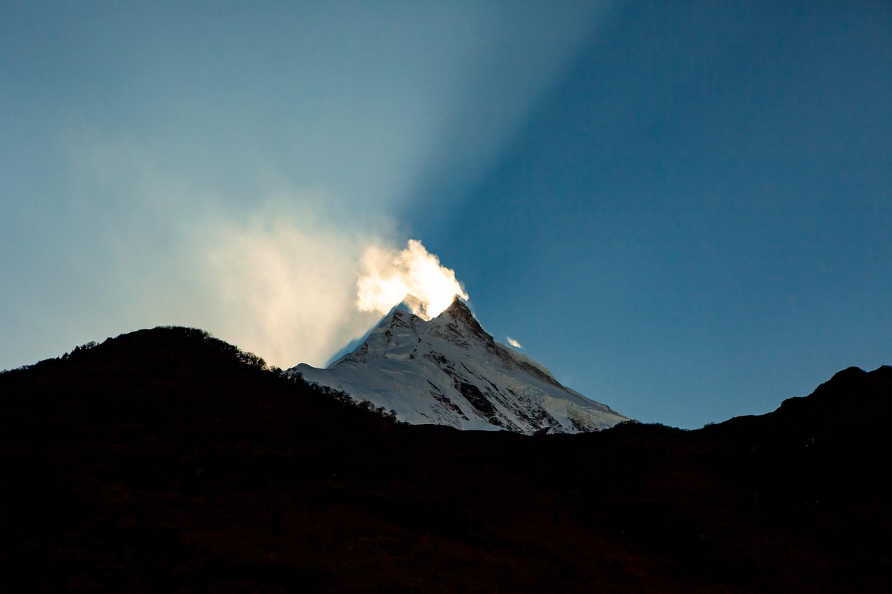 Sunrise over Mt. Manaslu with golden sunlight illuminating the snow-covered peak against a clear blue sky.