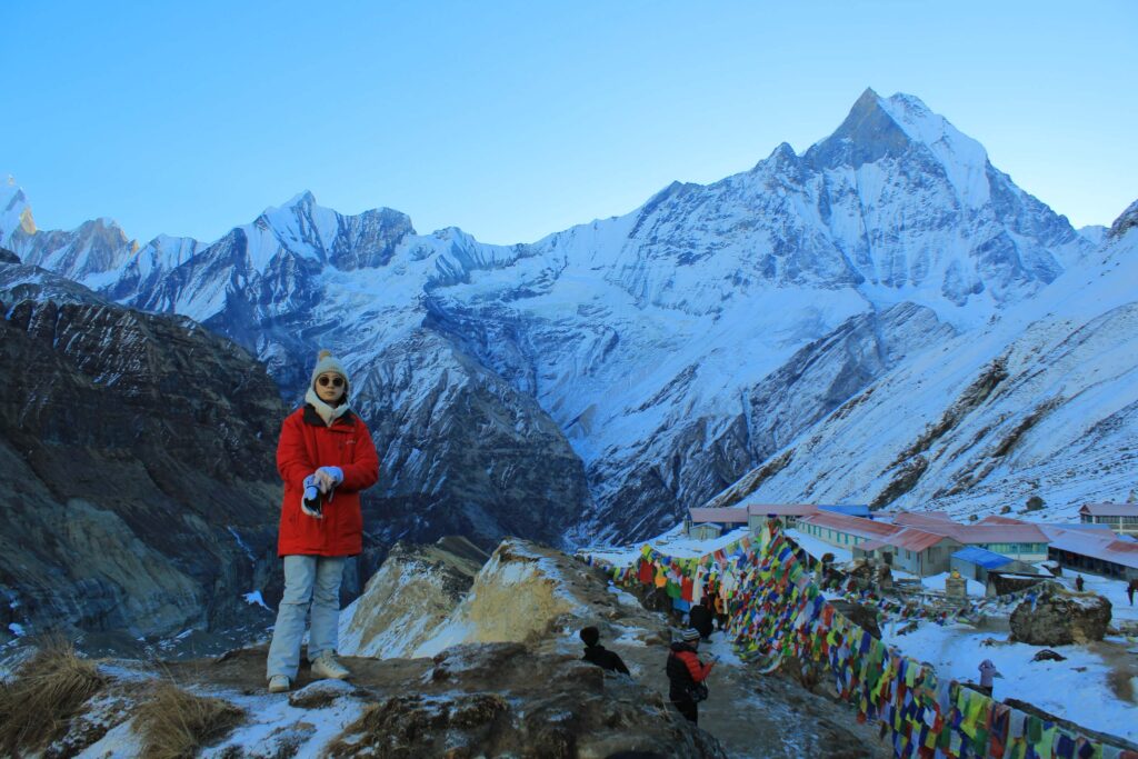 Trekkers at Annapurna Base Camp viewpoint with Mount Machapuchare and tea houses in the background.