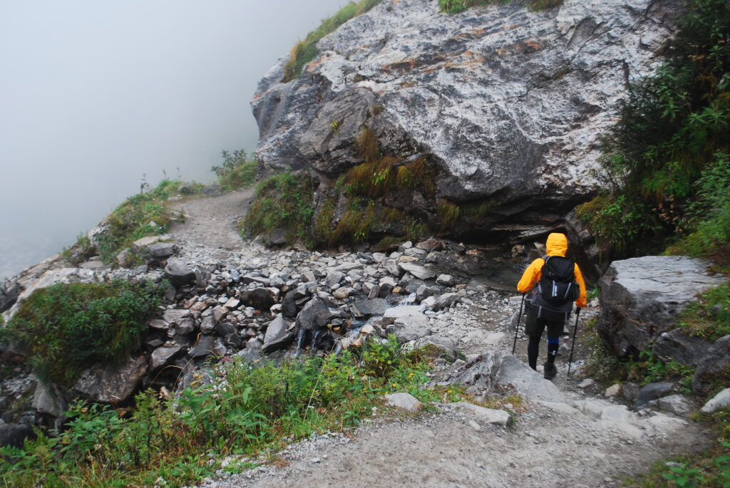 Trekker walking alone on a foggy mountain trail in Himalaya Durali, surrounded by mist and rugged terrain.