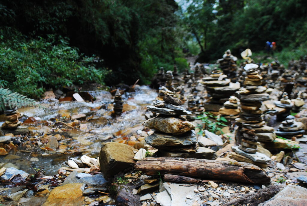 Stacked mani stones with Buddhist inscriptions arranged on a riverbank beside the Annapurna trekking trail.