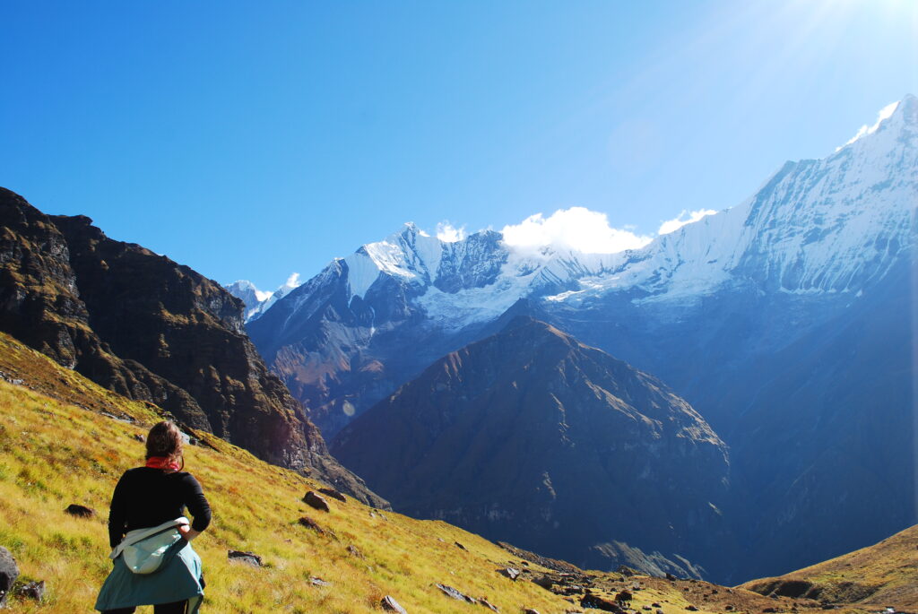 A lone trekker standing on a high viewpoint, gazing at the snow-covered peaks of the Annapurna mountain range.